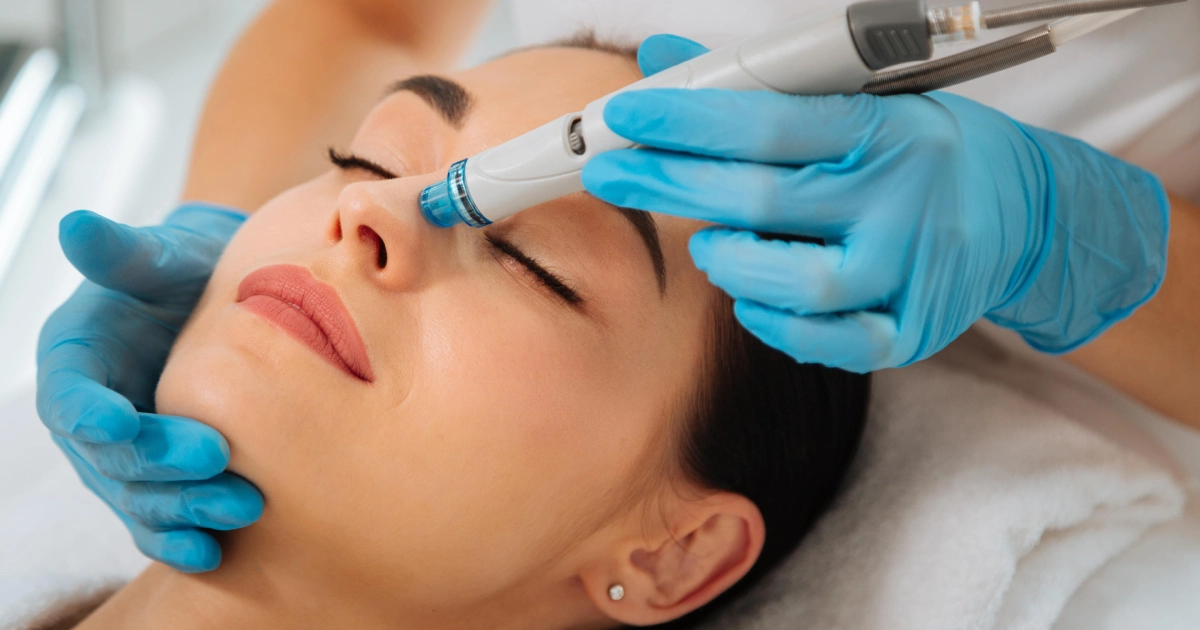 Close-up of a woman receiving a HydraFacial in Bellmore, NY, with eyes closed as a professional in blue gloves applies a handheld device to her nose.